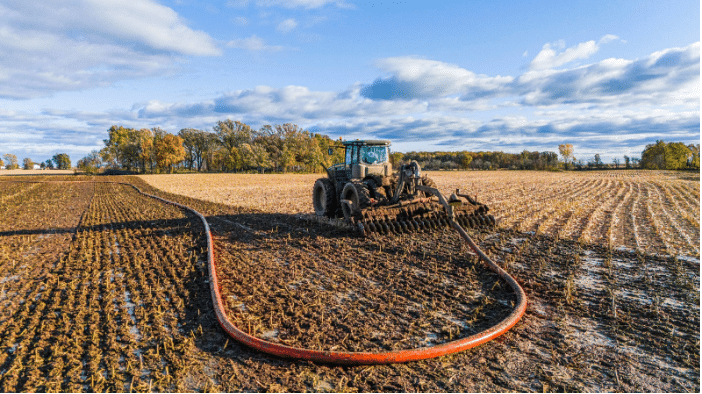 Tractor applying manure with dragline pumping system for efficient nutrient application in farmland.