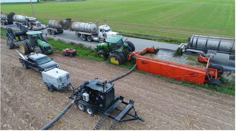 Modern dragline manure pumping system with tractors, trucks, and hoses working for efficient field application.