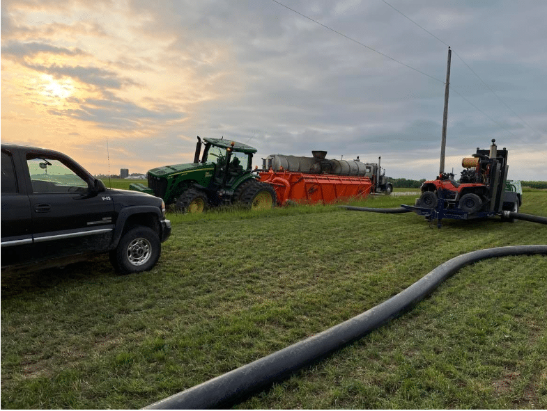Tractor and dragline manure equipment pumping system in a farm field during sunrise for efficient nutrient application.