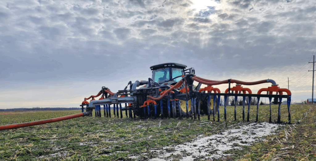 Tractor with dragline toolbar applying liquid manure in a field, featuring hoses for injection and top-spreading application.