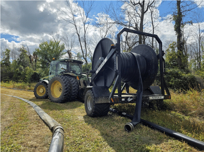 Tractor pulling hose reel system used for manure pumping operations in the field during maintenance checks.