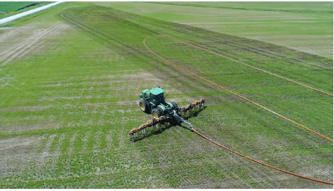 Tractor dragging Mandals hose applying manure across farmland for efficient nutrient distribution.