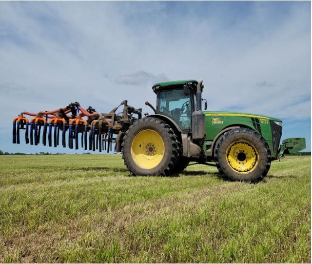 Heavy-duty tractor using dragline manure equipment with toolbar for efficient manure application in open farm field