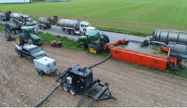 Full manure drag hose system with tractors, tankers, and pumping equipment operating in a crop field.