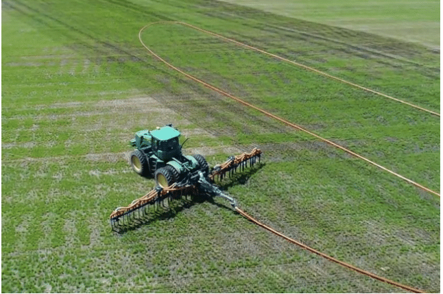 A tractor applying manure using a dragline system with Mandals drag hose across a green crop field.